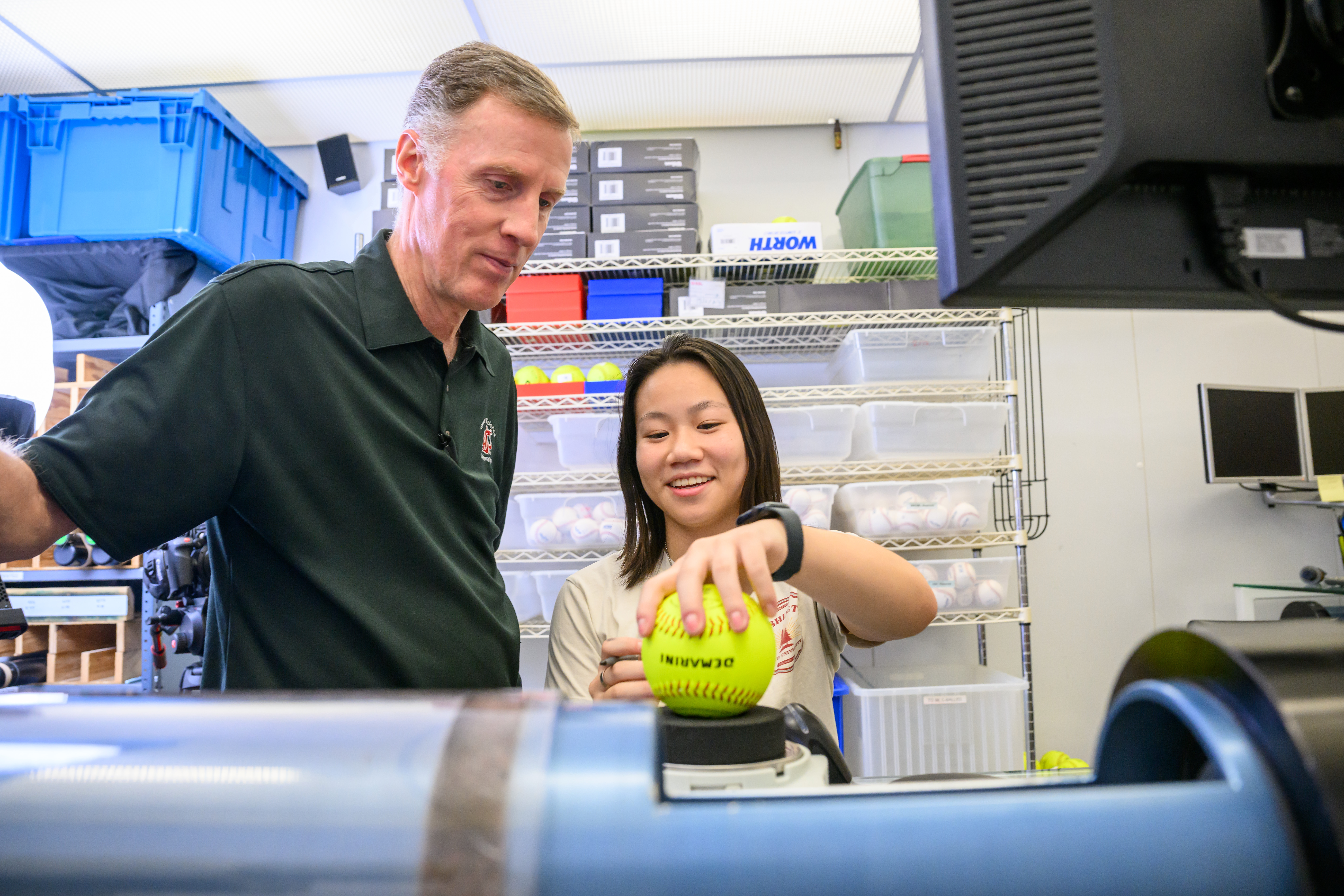 Two people testing a softball on measuring equipment.