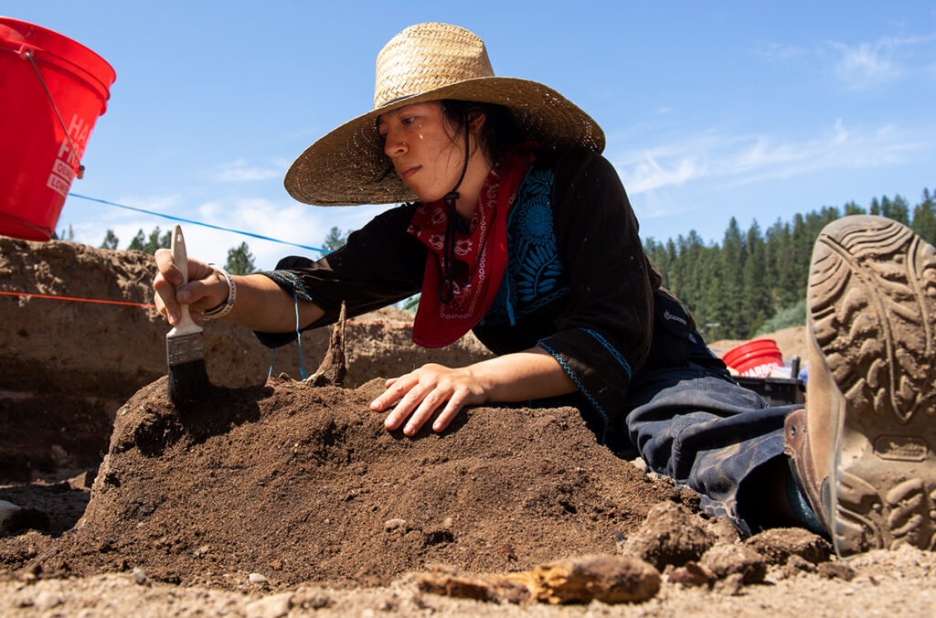 A person using a brush to move soil during an archeological excavation.