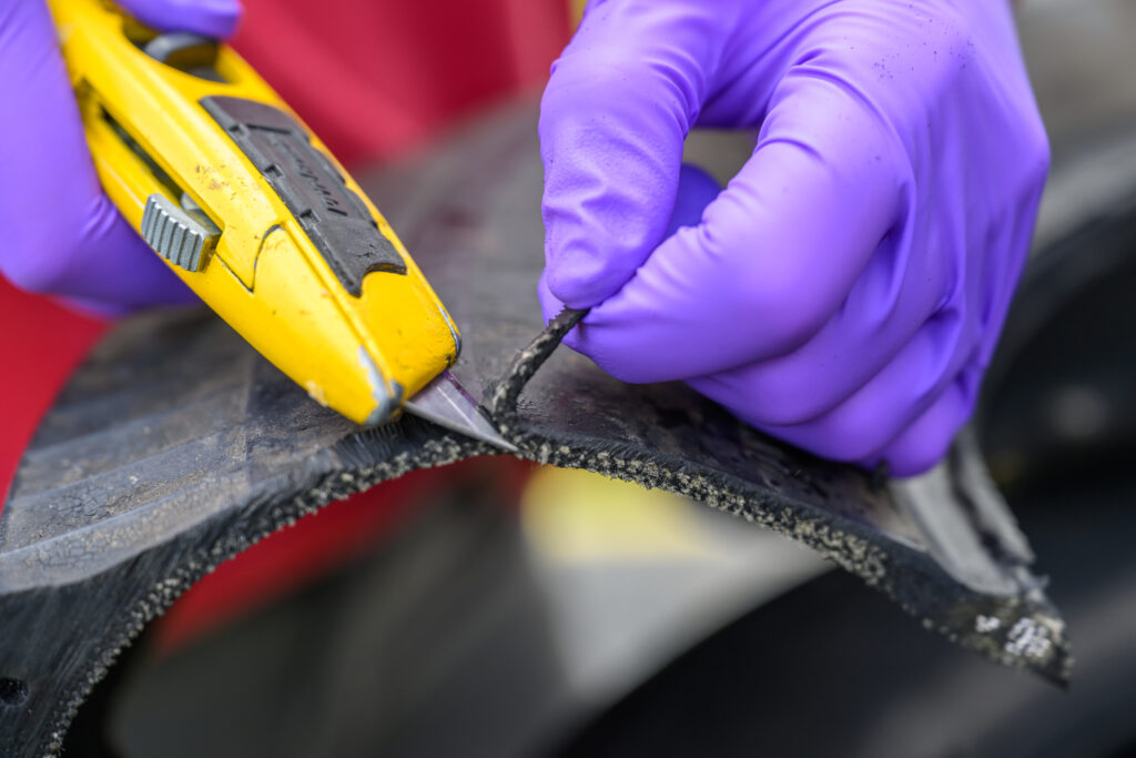 Closeup of a person cutting a piece off of tire material.