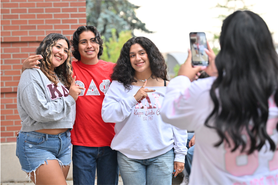 Three people wearing Greek-life shirts posing for a photo with the photographer in the foreground.