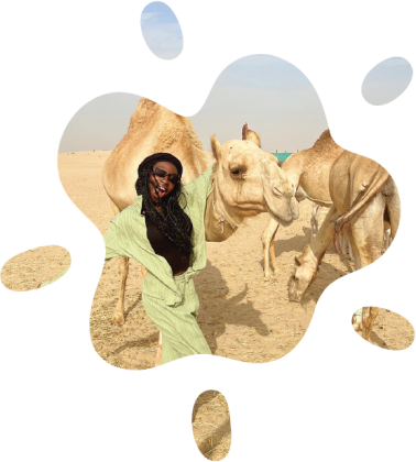 A smiling person posing dramatically with their arm on a camel's neck.