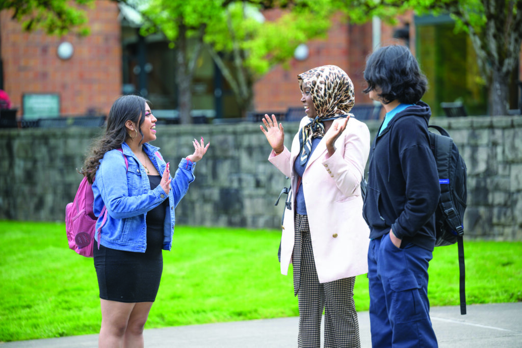 WSU Vancouver-Undergraduate advising | Two staff members chatting next to an outdoor lawn area on a sunny day at WSU Vancouver