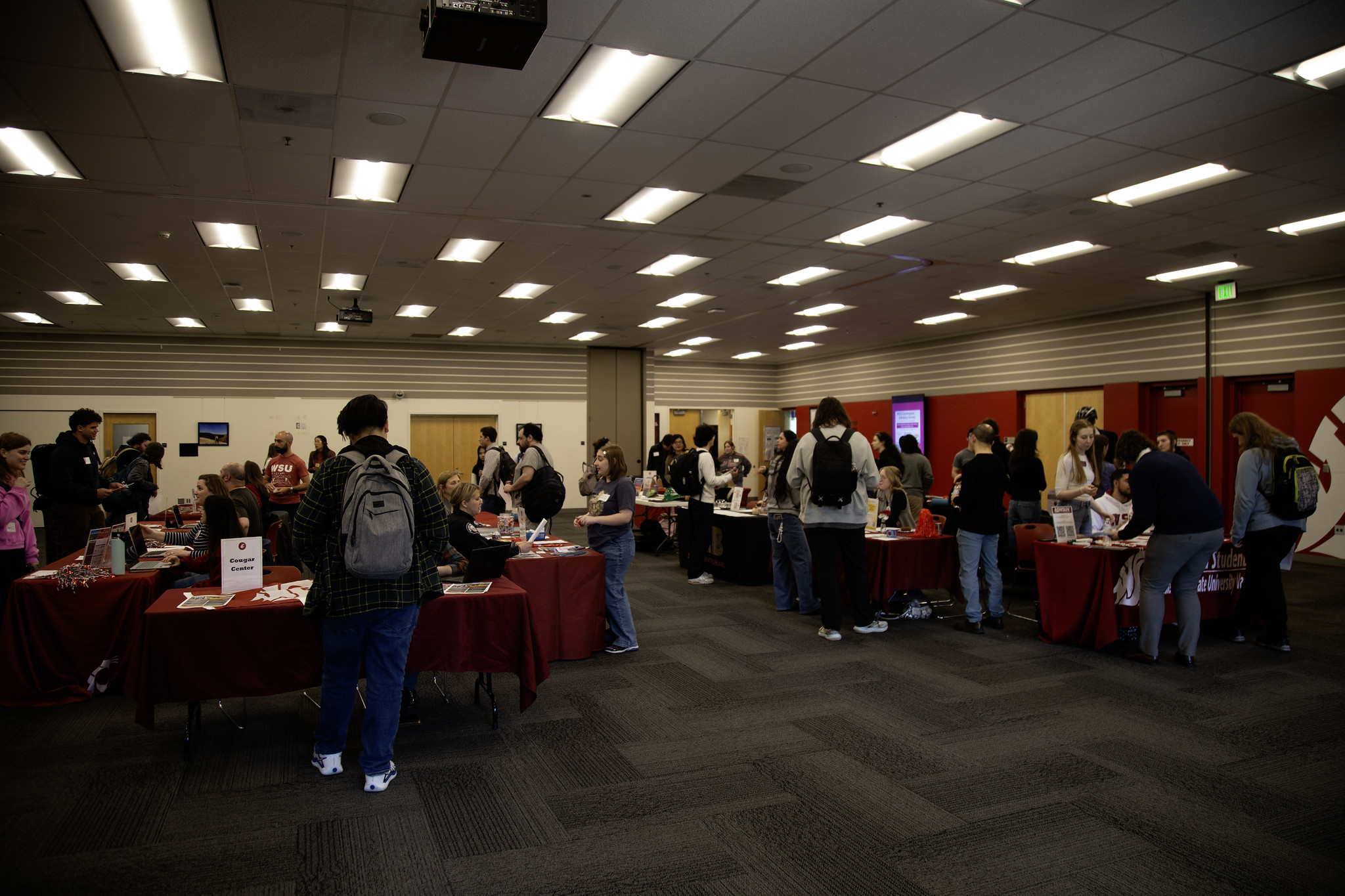 A group of individuals browsing through books and materials at a WSU Vancouver indoor market bazaar