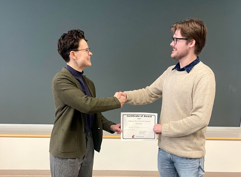 Two professional colleagues shaking hands during a graduation or award presentation ceremony indoors