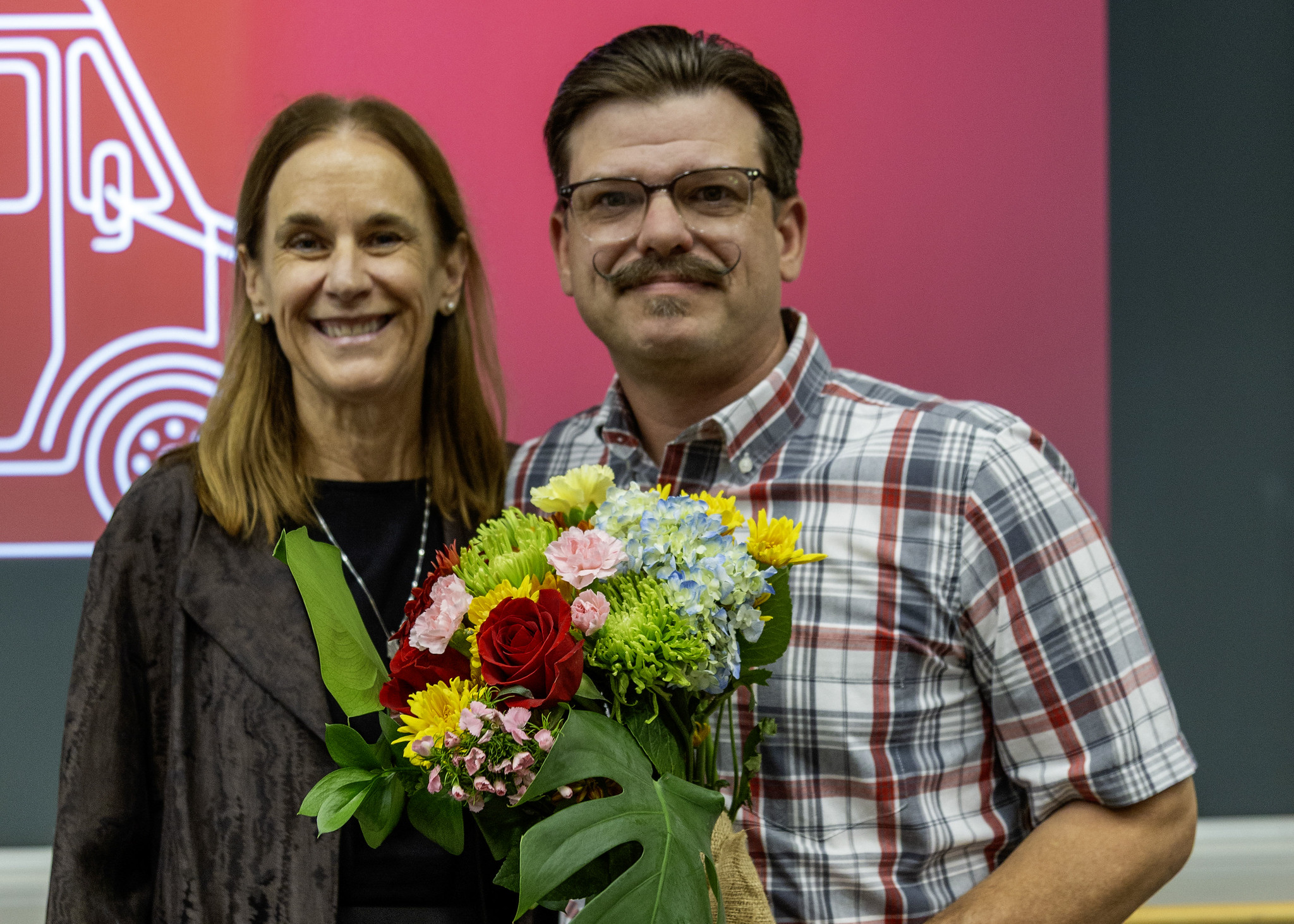 A smiling couple posing together while holding a vibrant bouquet of fresh flowers