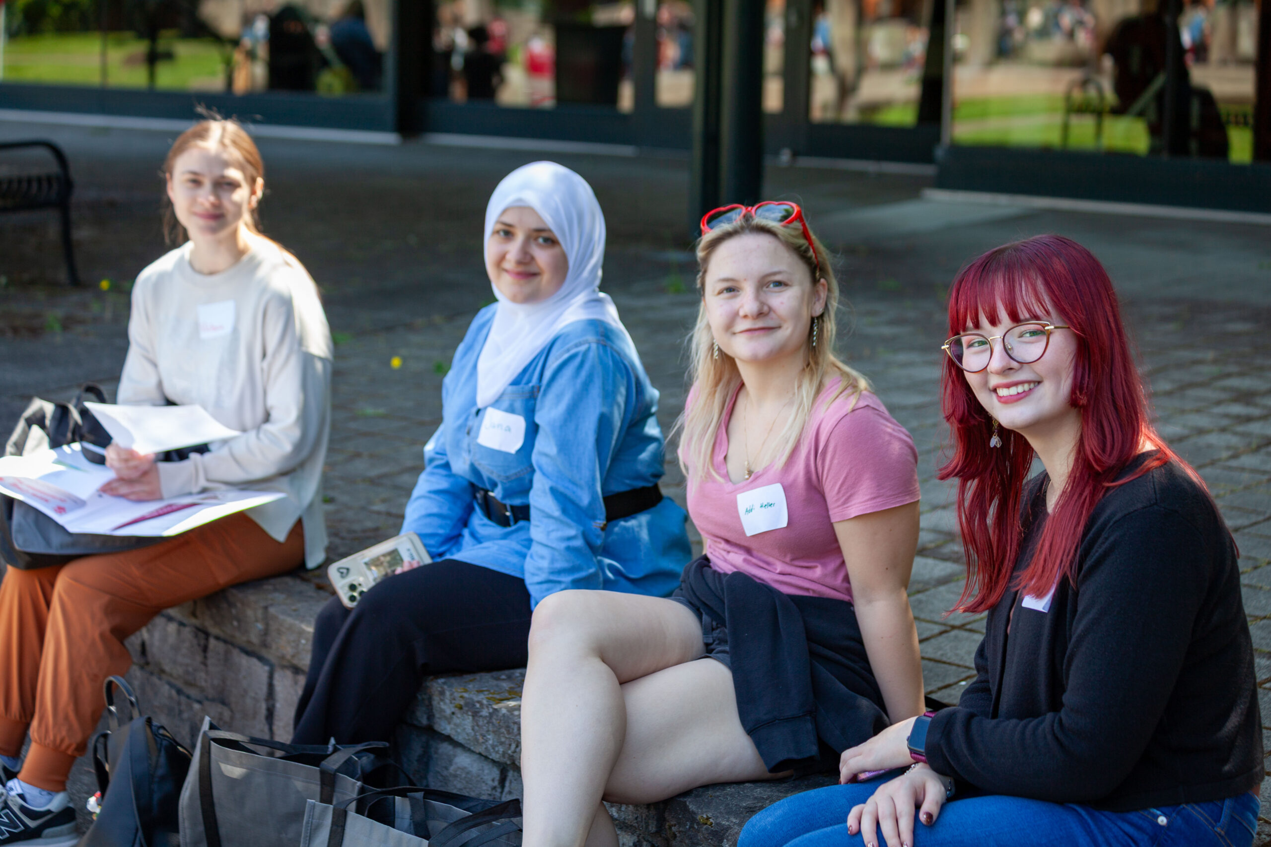 Three young women sitting together on an outdoor stone ledge laughing