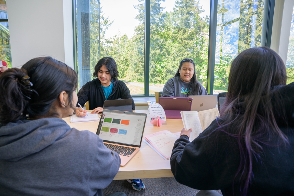 A group of students working and studying together around a table with laptops