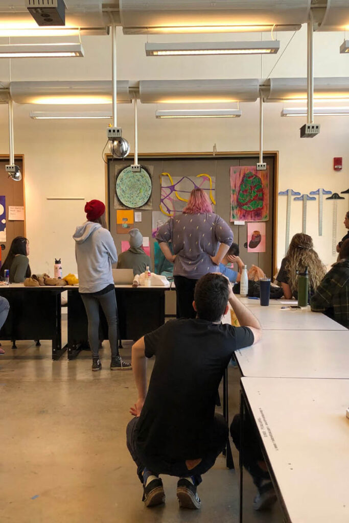An indoor classroom workshop with a presenter standing near a chalkboard