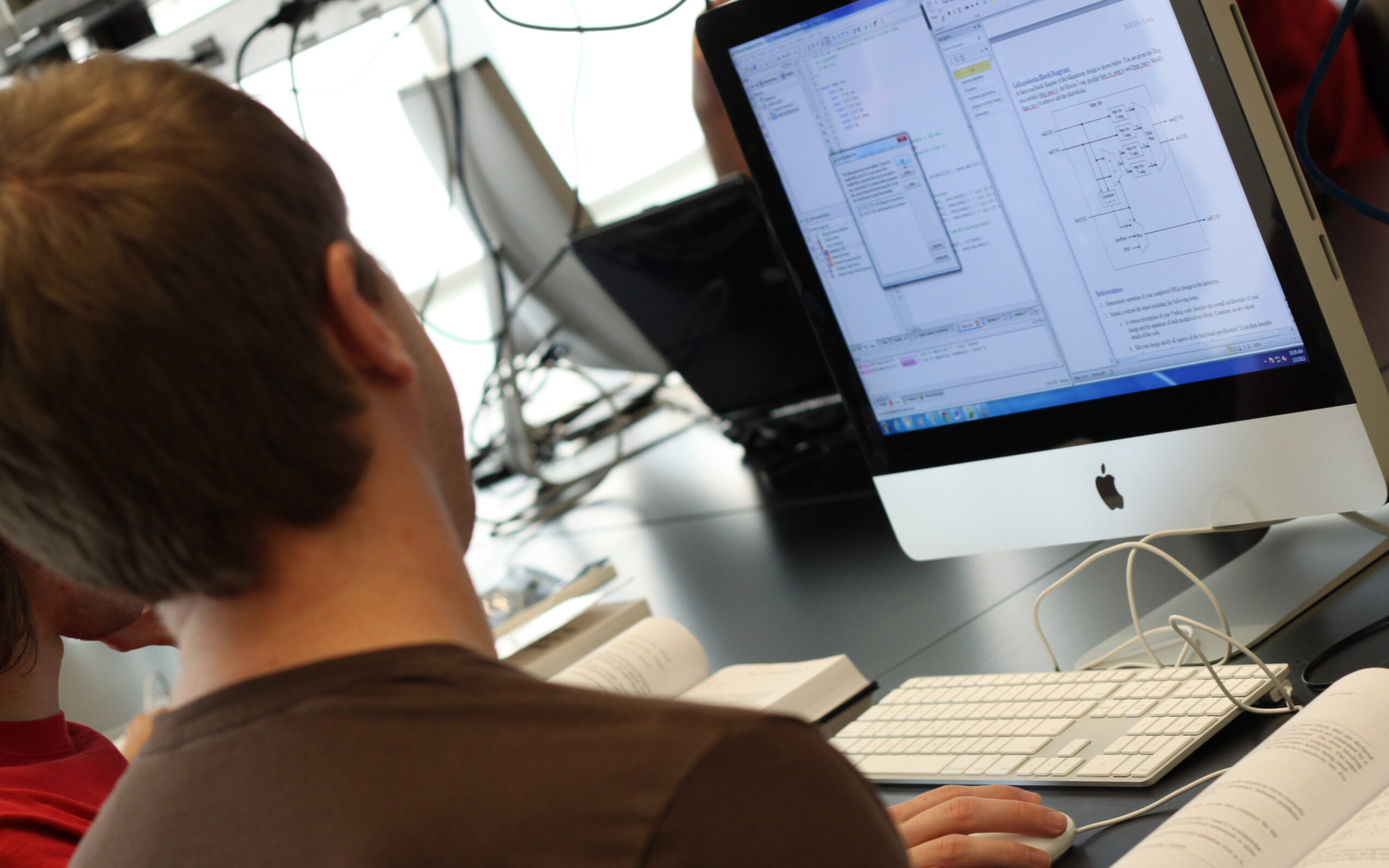 An over-the-shoulder view of an engineer monitoring code across multiple screens at WSU Vancouver
