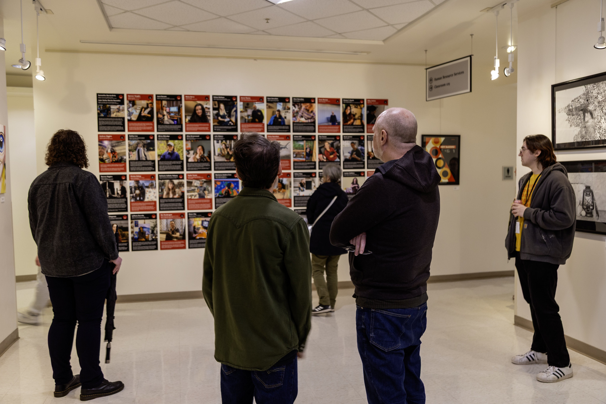 Two people examining a grid wall of photography prints in a gallery space