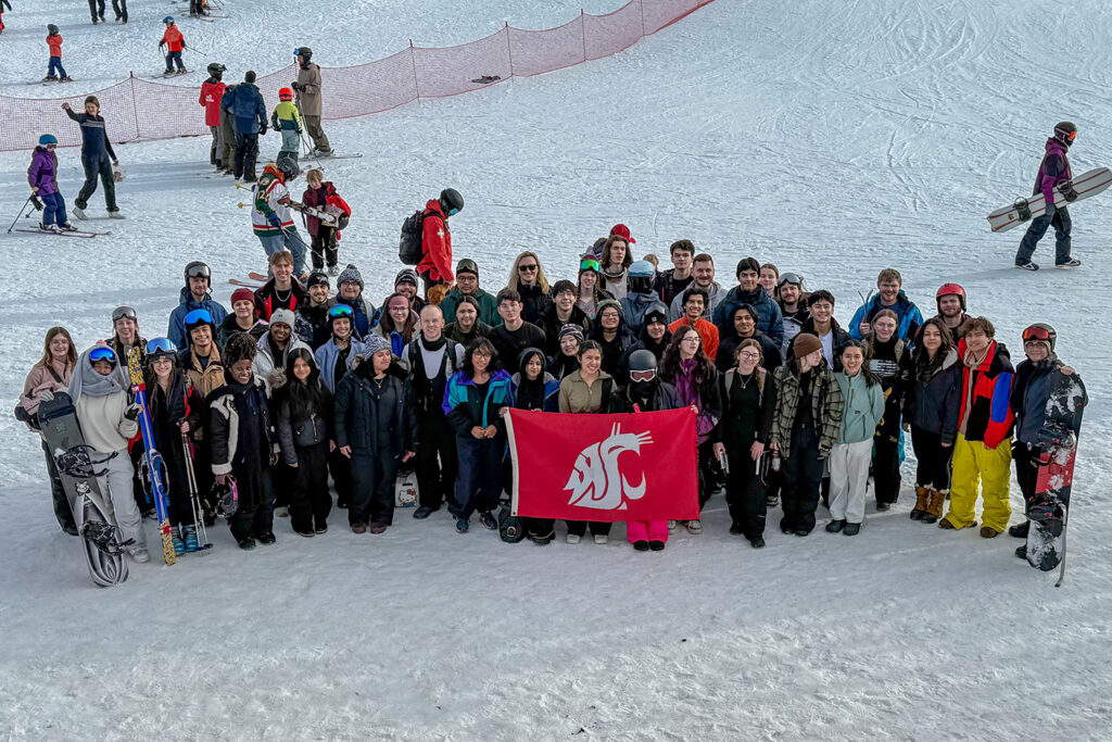 WSU Vancouver-Study Abroad | A large group of students posing with a crimson WSU flag on a snowy field trip