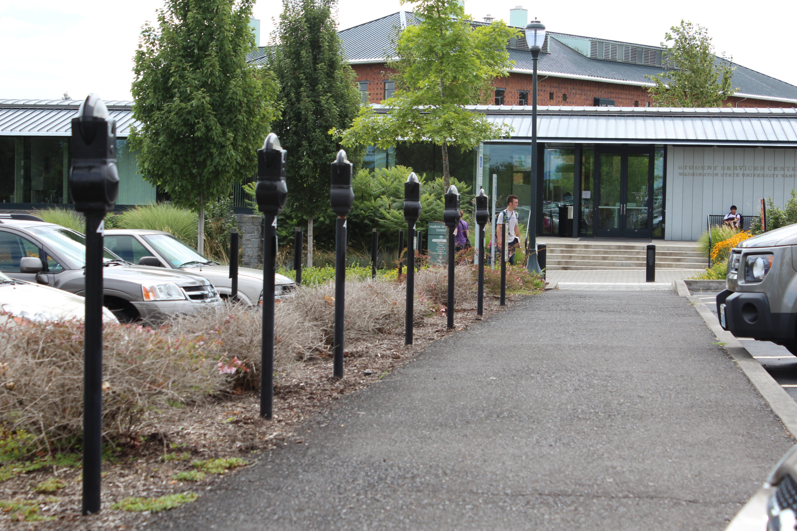 A sidewalk path lined with black parking meters leading toward a modern campus building entrance.