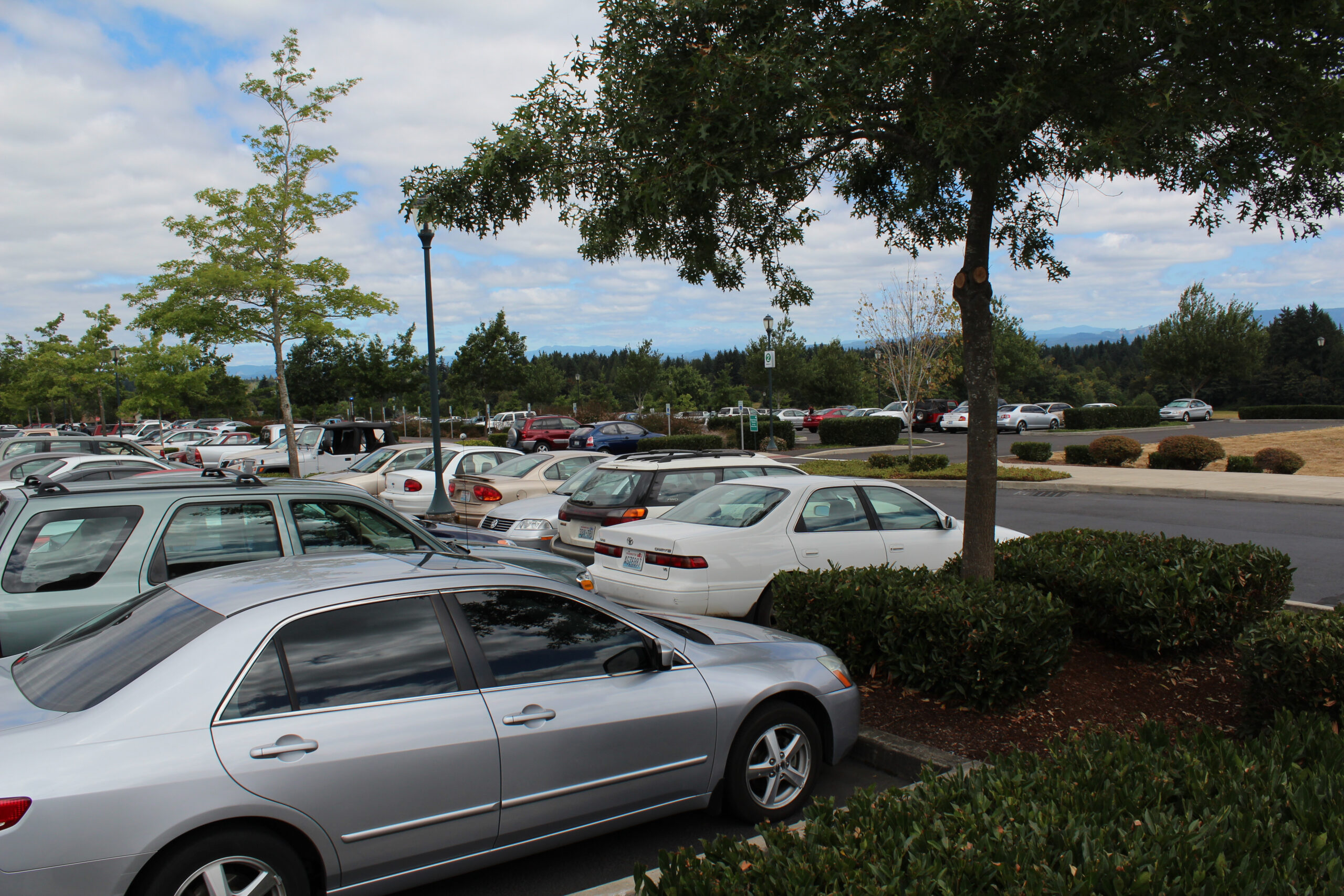 A wide view of a crowded campus parking lot filled with various cars on a partly cloudy day.