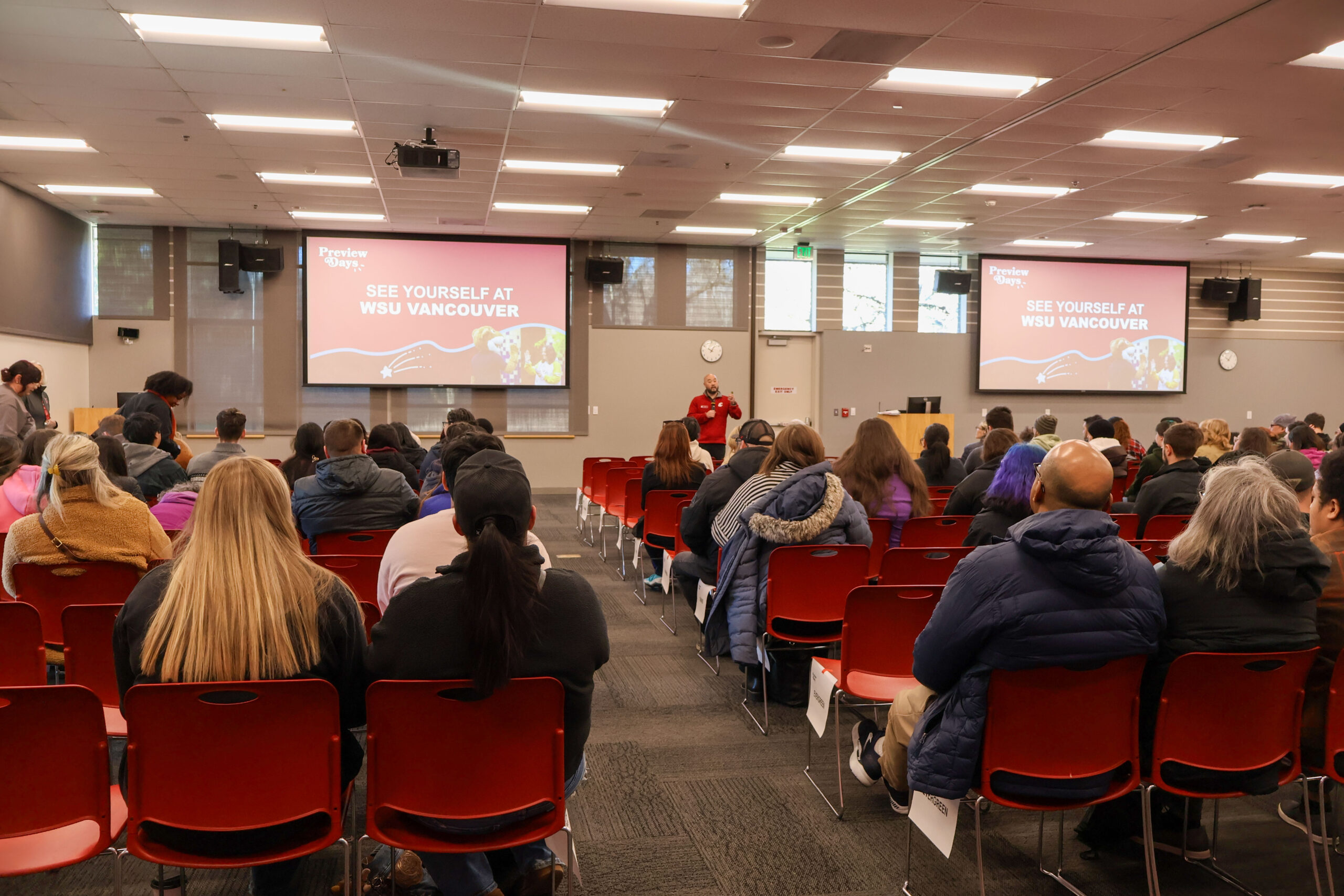 An audience sitting at rows of conference seats watching an educational lecture presentation indoors