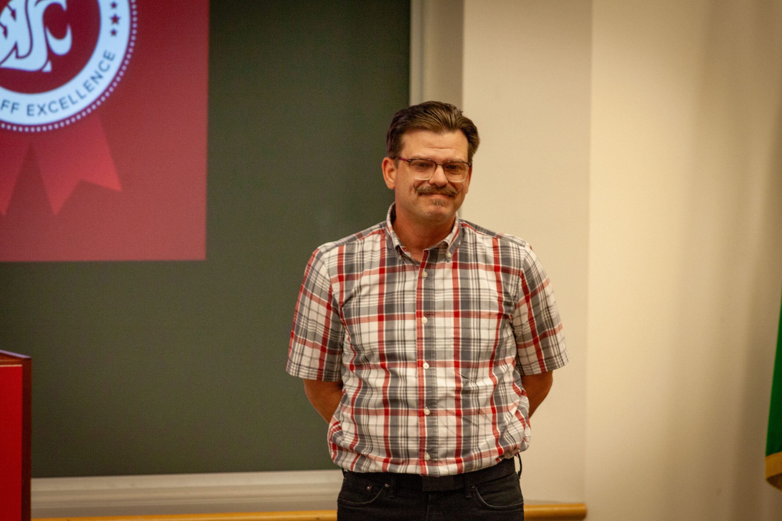Portrait of a smiling WSU Vancouver faculty member in a plaid shirt inside a classroom