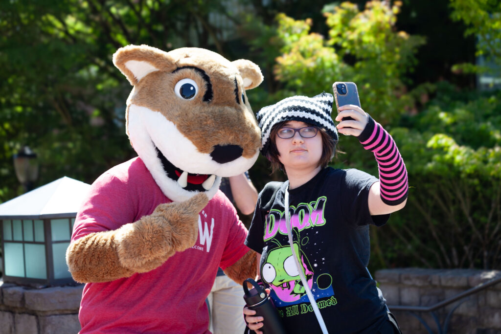 WSU Vancouver-Academic Petitions | A student photographer holding a camera and smiling during an outdoor campus event