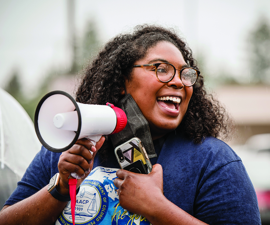 A cheerful WSU Vancouver student leader shouting enthusiastically into a megaphone at an outdoor campus event