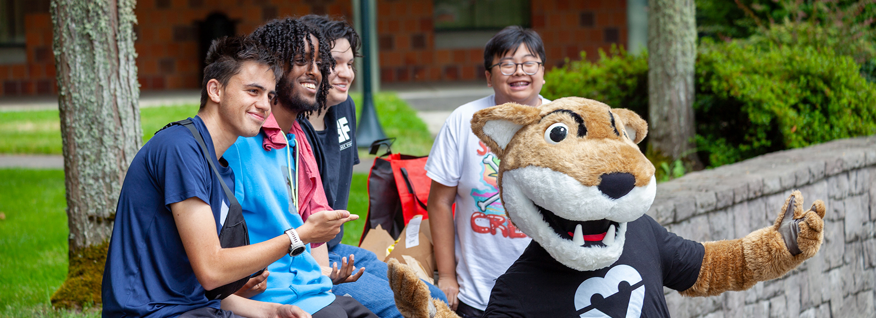 Students posing for a photo with Butch, the WSU mascot, near a brick campus structure