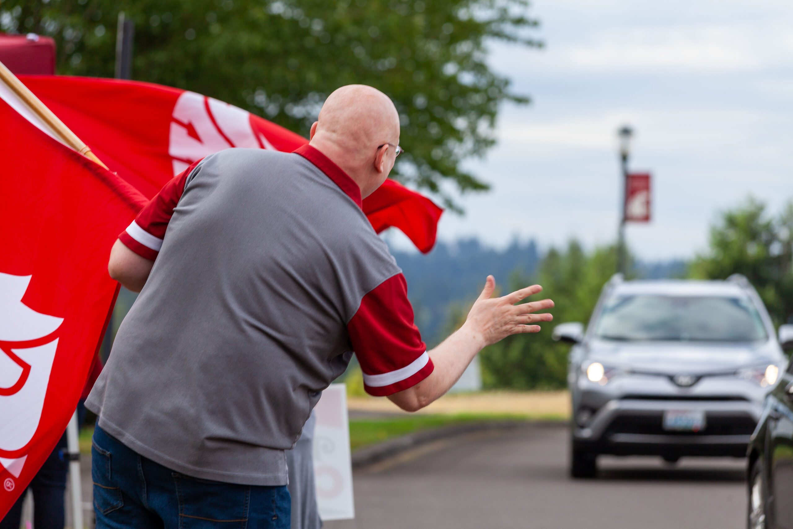 Parking Services A student wearing a red jacket waving to someone from a campus pathway outdoors