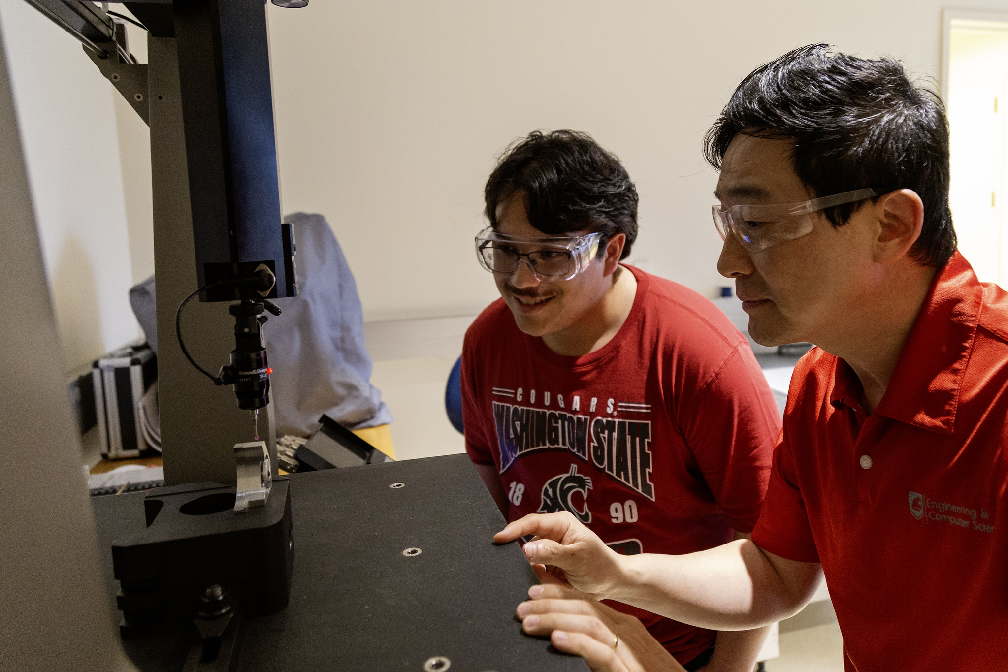 Two individuals interacting with an interactive display screen or testing console in a lab