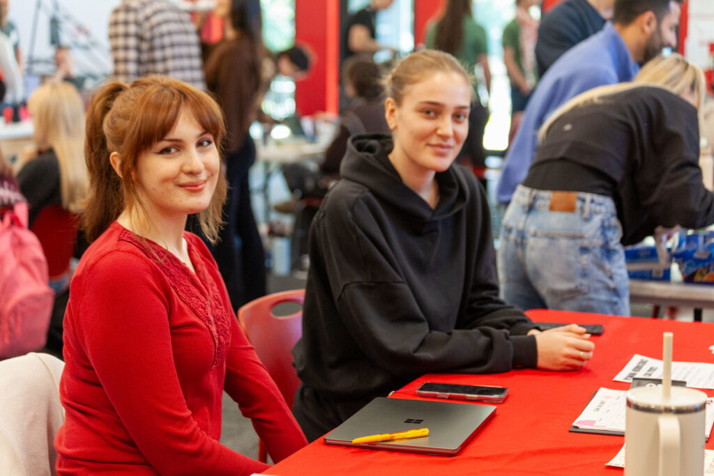 Two young women sitting at a table with red decoration talking
