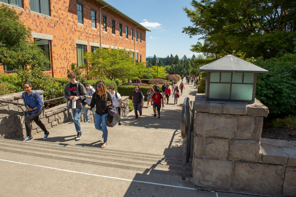 Students walking along a paved pathway on campus next to brick buildings