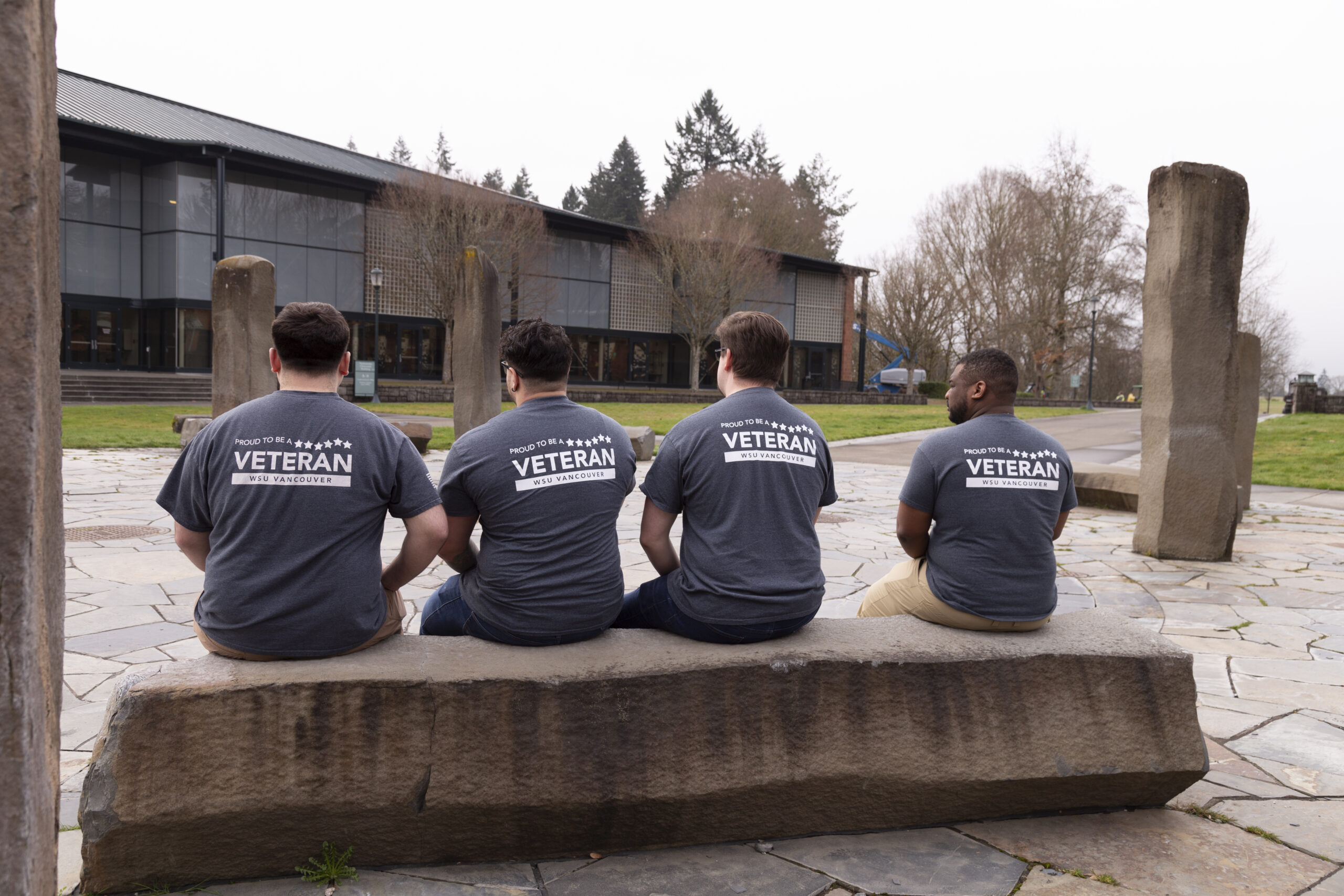 Veteran and Military-Affiliated Student Services - WSU Vancouver | A row of student veterans wearing matching group shirts sitting together on an outdoor stone bench
