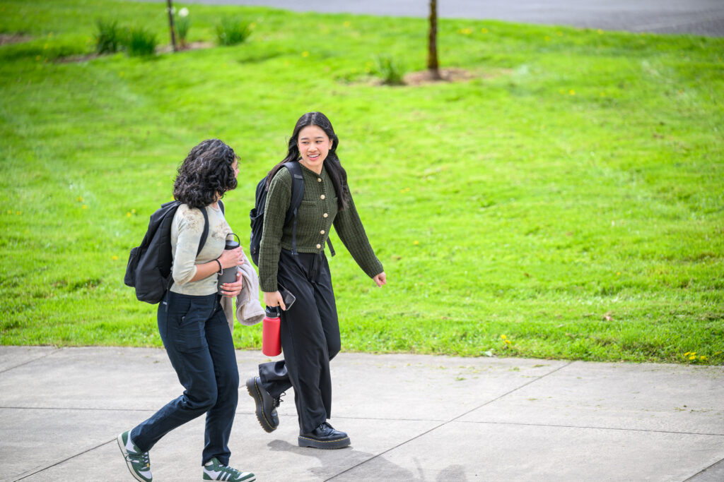 Two students walking down an outdoor campus path next to modern brick academic buildings