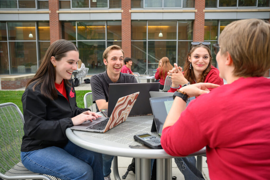 Students collaborating on a laptop at an outdoor patio table on the WSU Vancouver campus