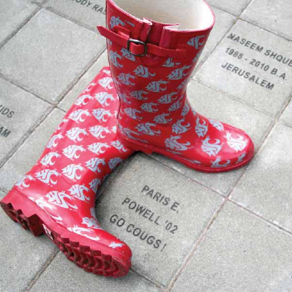 A stylized red and white patterned rain boot sculpture displayed outdoors on a brick pathway