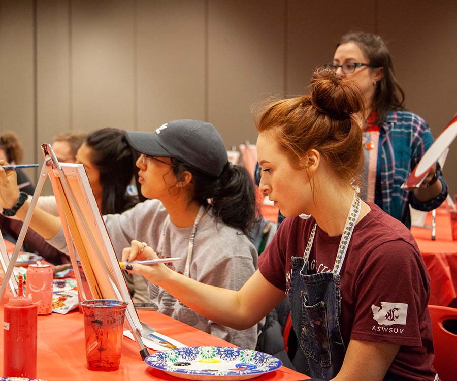 Students paint on small table easels during an indoor campus art event at WSU Vancouver.