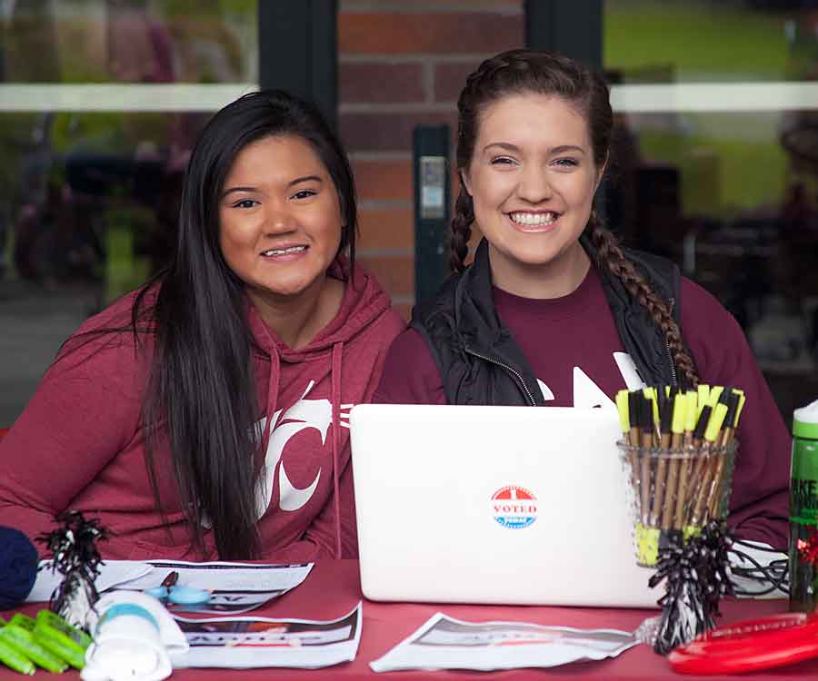 Two professional women discussing resources at an indoor informational booth table