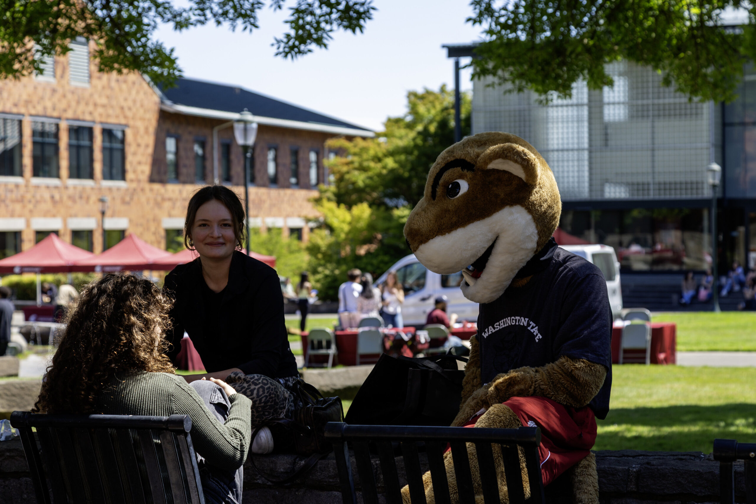 Two students sharing a laugh while sitting down with Butch, the WSU mascot, on campus grounds