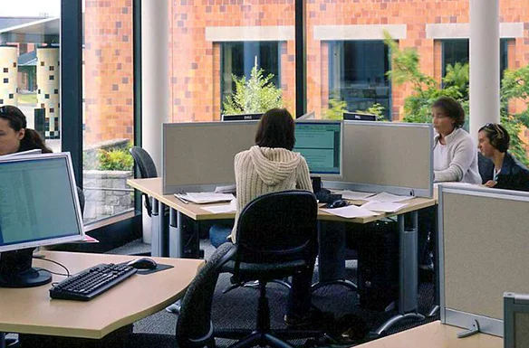 Students working at computer stations in a bright, modern library or computer lab with large windows.