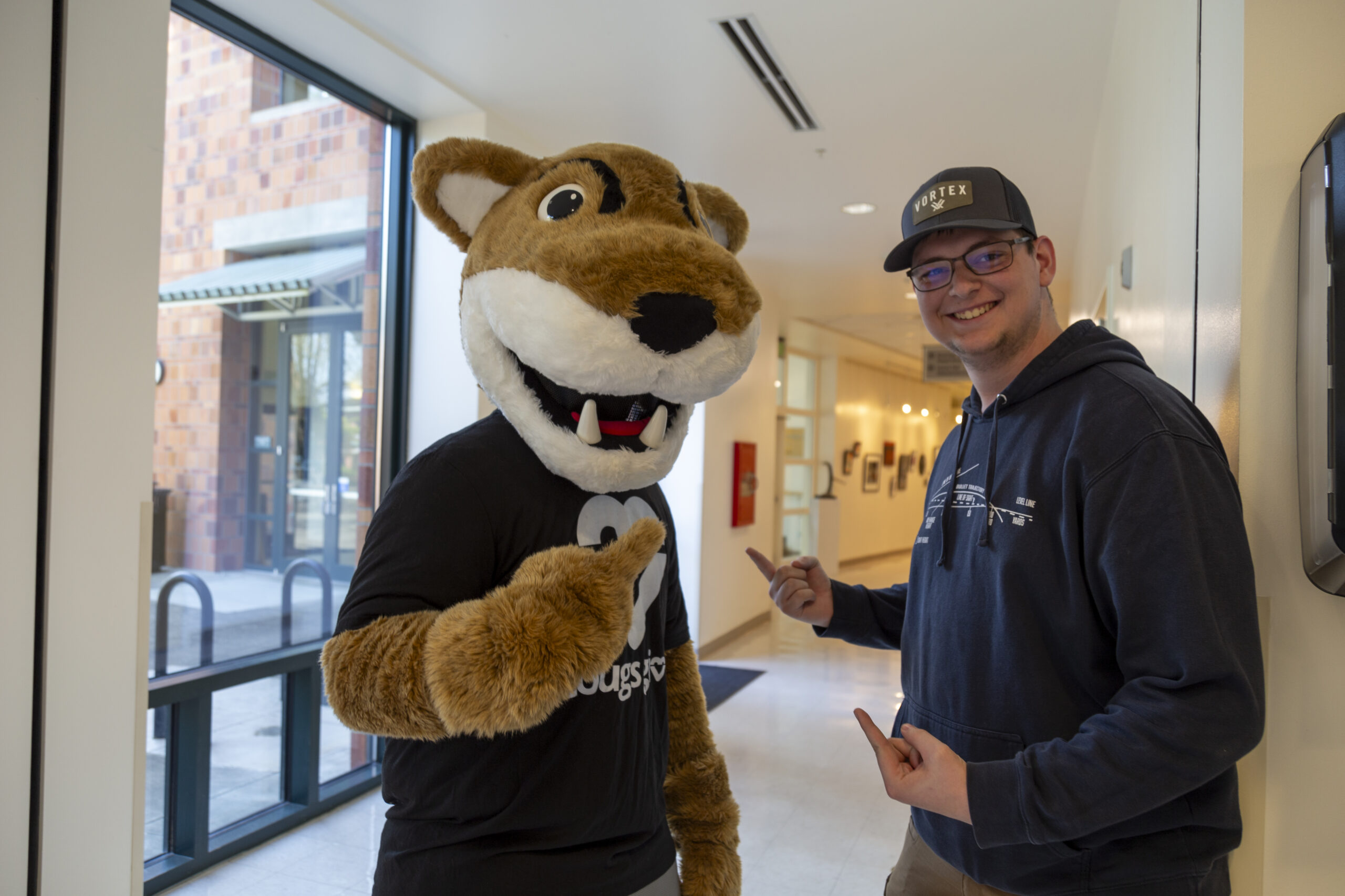 A person interacting cheerfully with a cougar mascot outside