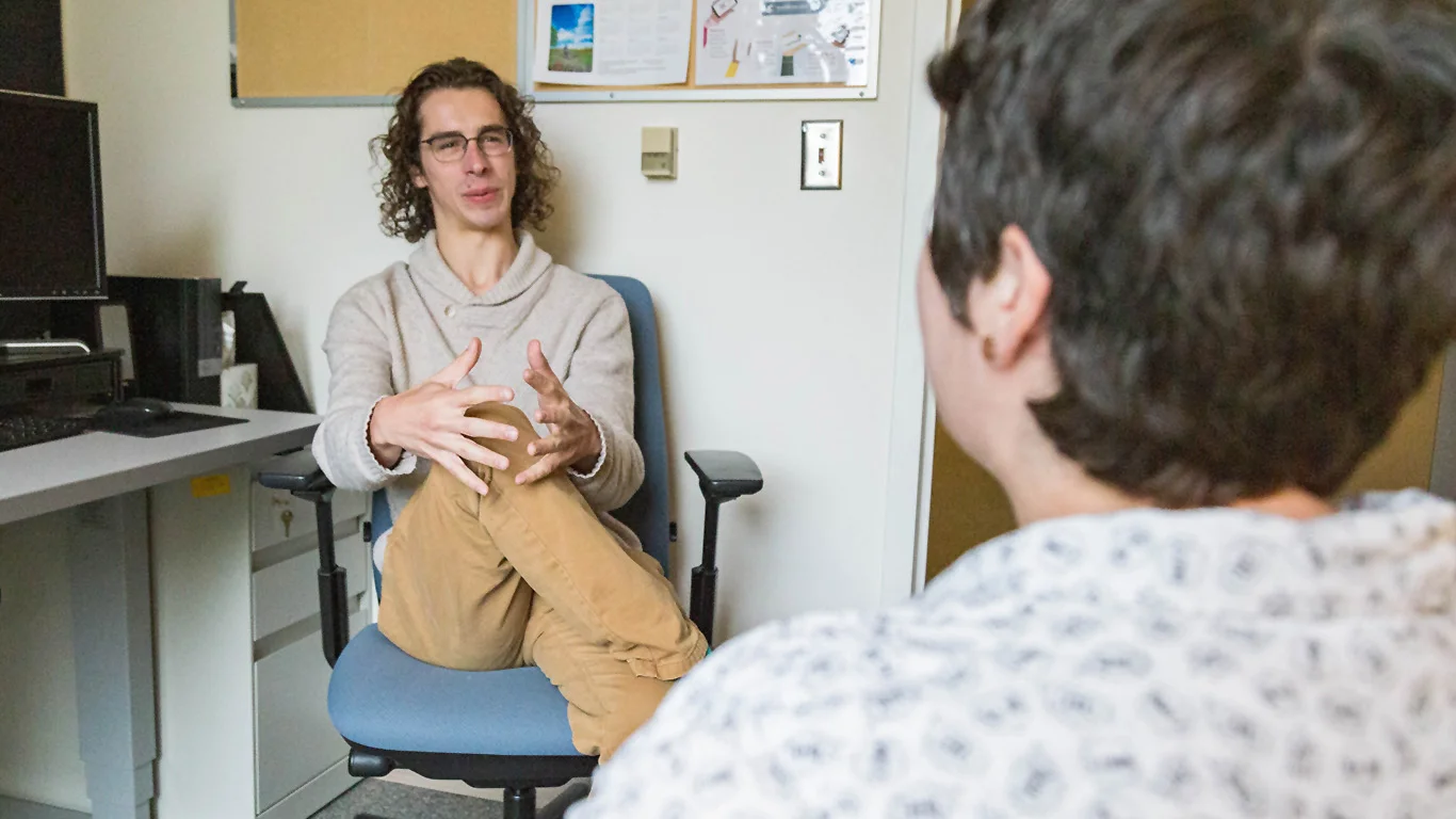 A man in a casual outfit sitting and talking in an office or lounge space