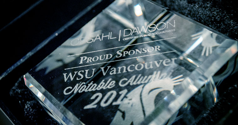A clean glass award plaque celebrating a WSU Vancouver Notable Alumnus on a textured background