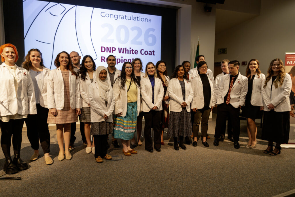 A group of medical or nursing graduates in white coats posing together under an event banner