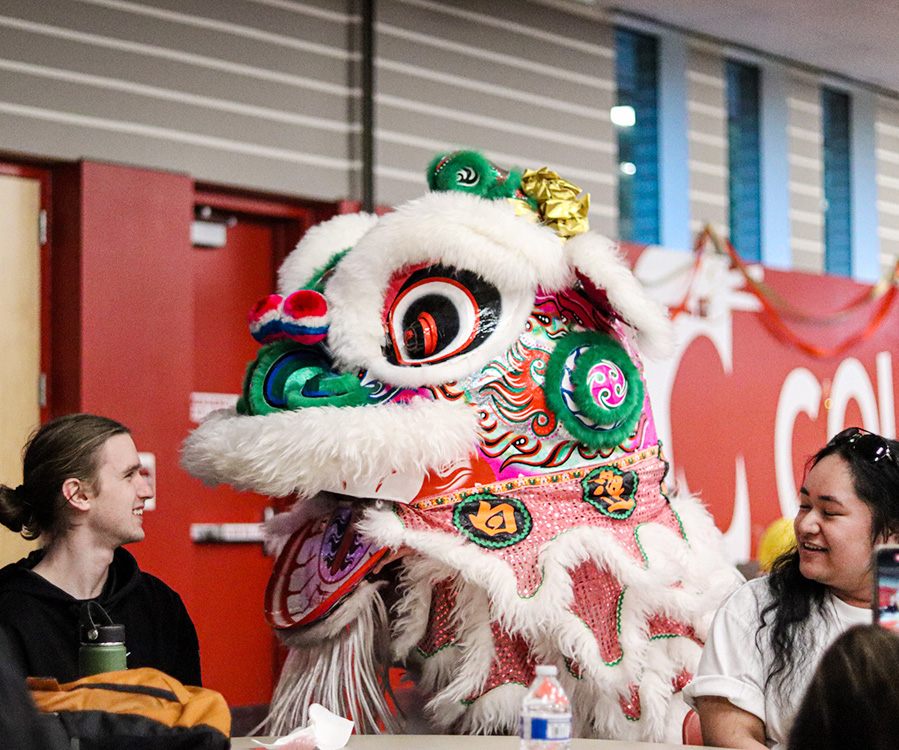 A performer operating a colorful red and white traditional dragon costume during a campus parade celebration