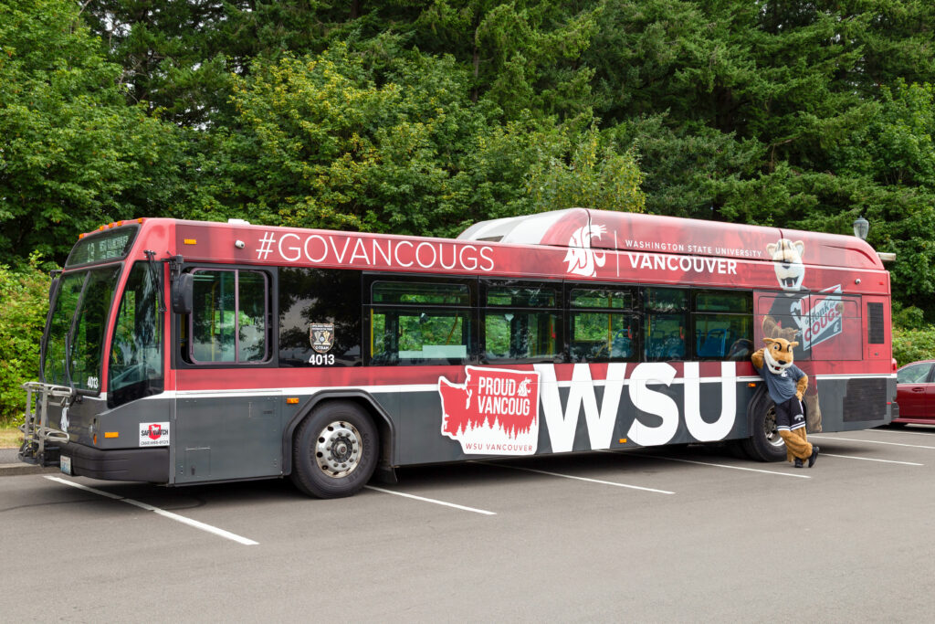 A red WSU Vancouver campus shuttle bus parked at an outdoor transit stop