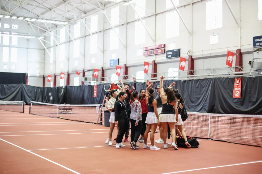 A group of volleyball players standing in a huddle on an indoor sports court cheering together
