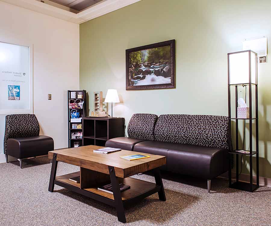Student Wellness Center - Counseling Services - WSU Vancouver | A small meeting lounge layout with a modern couch, coffee table, and large window view