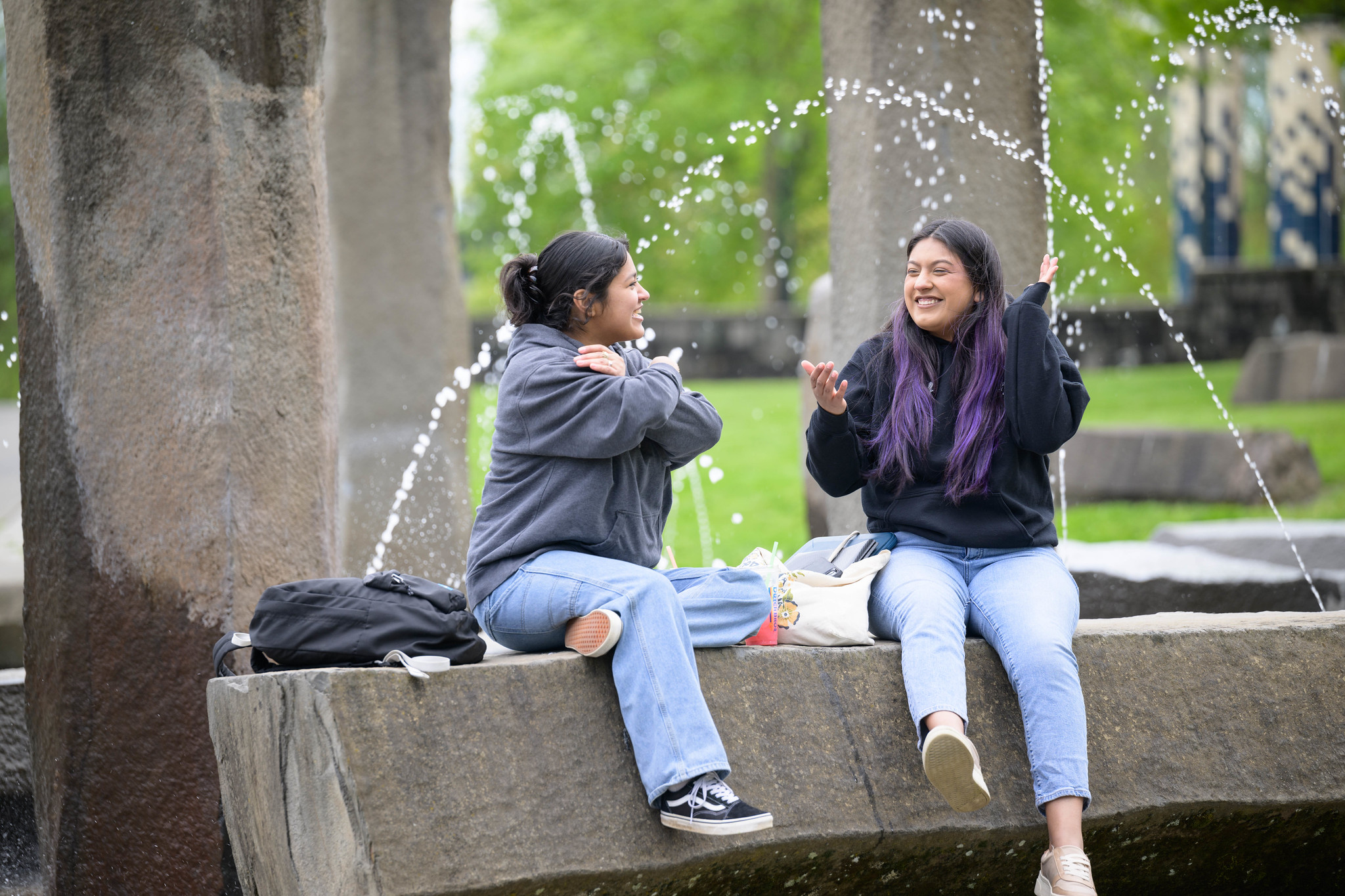 Two students relaxing next to an outdoor water fountain feature on campus