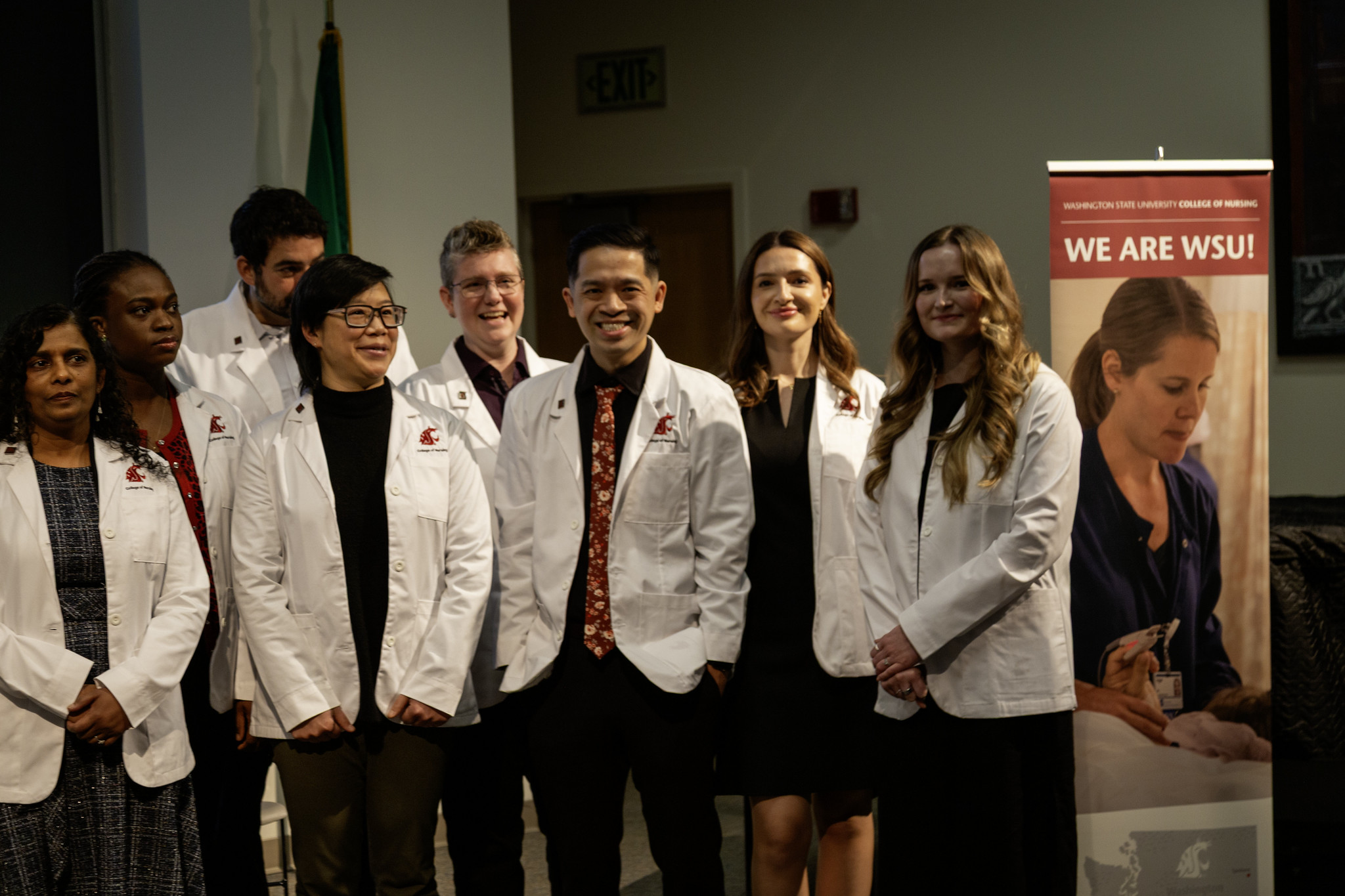 A group of medical students wearing matching white laboratory coats posing together in a classroom
