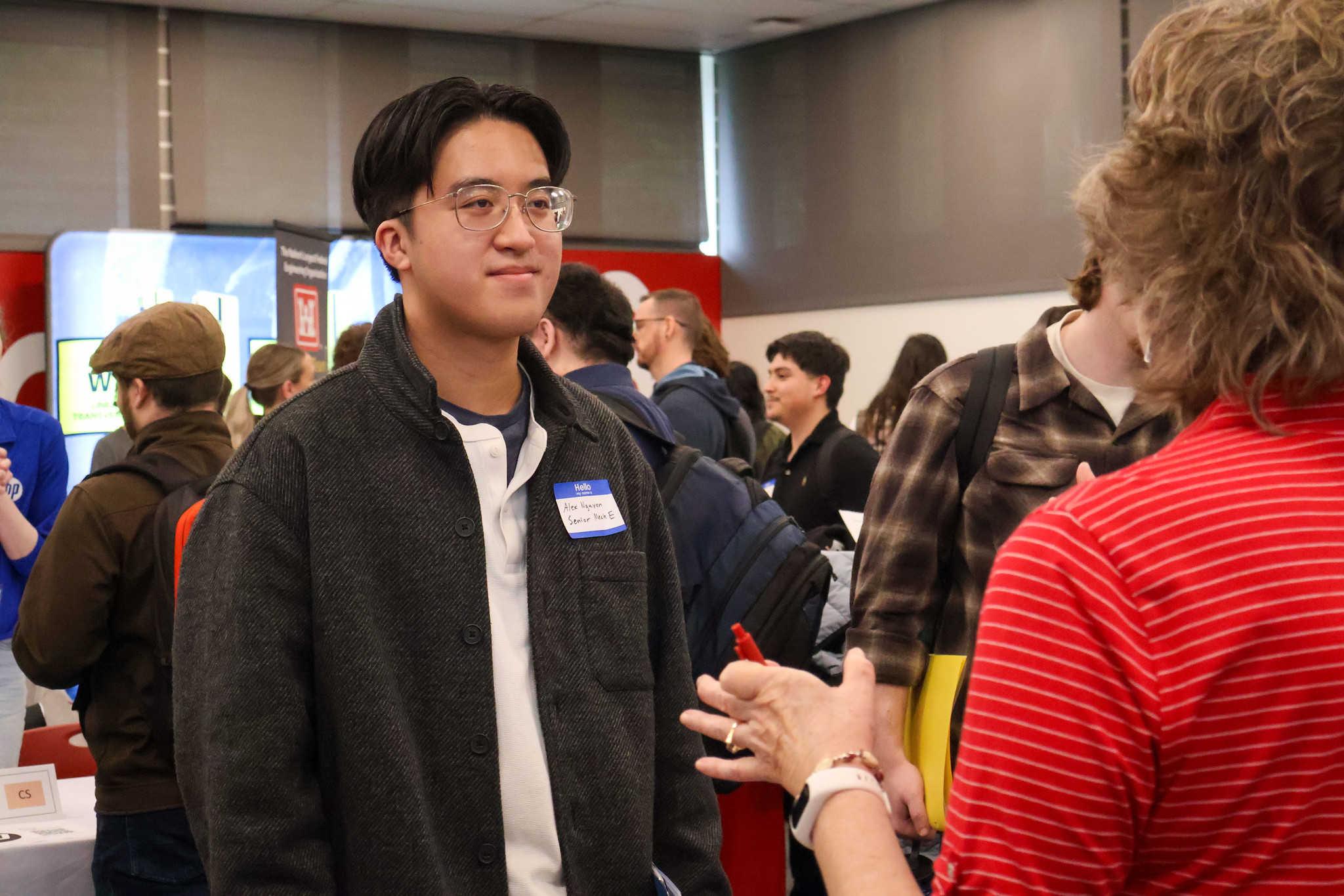 Portrait of a young male student wearing a name tag smiling warmly at a WSU Vancouver event