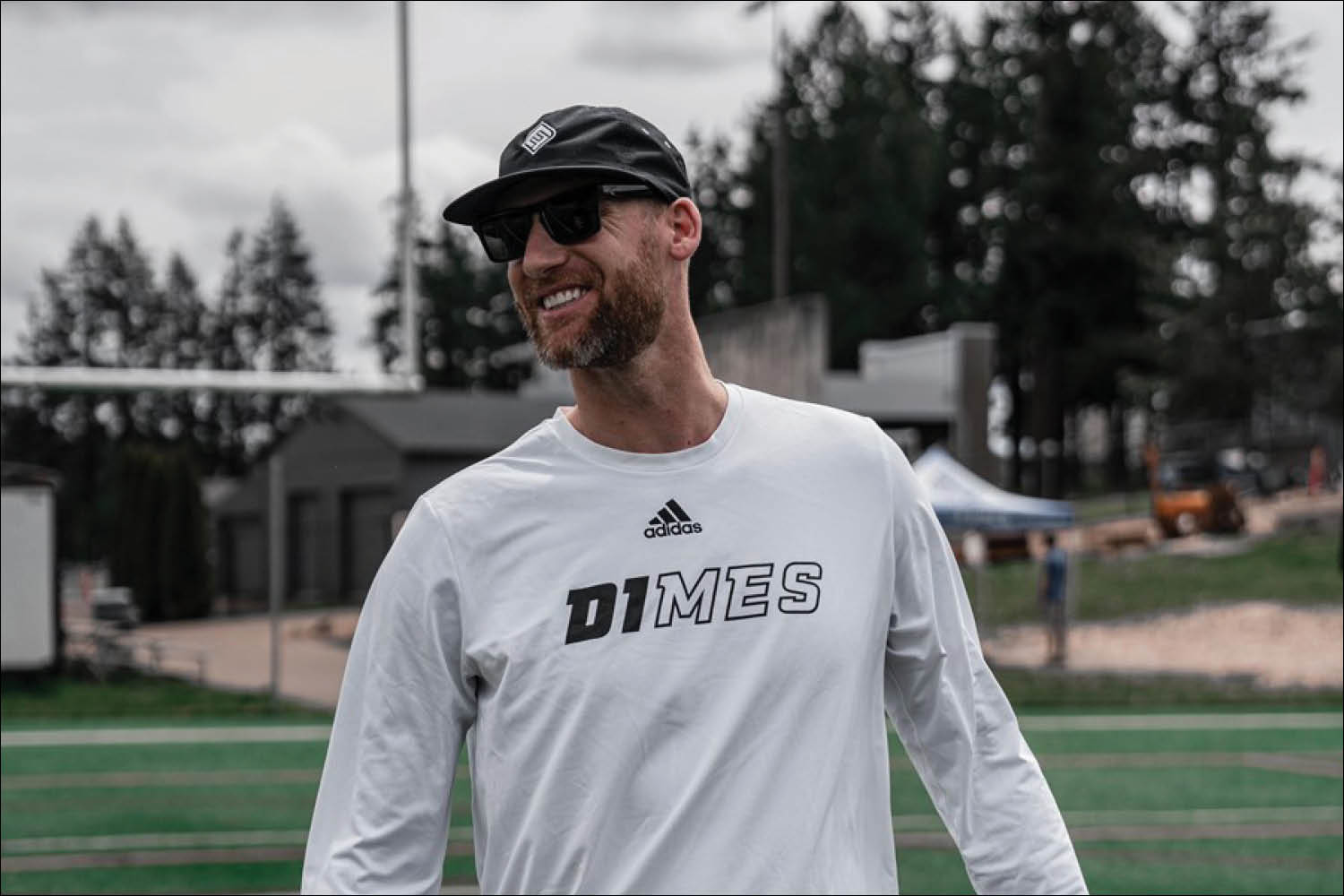 A man in a athletic cap and white shirt smiling on a sports field