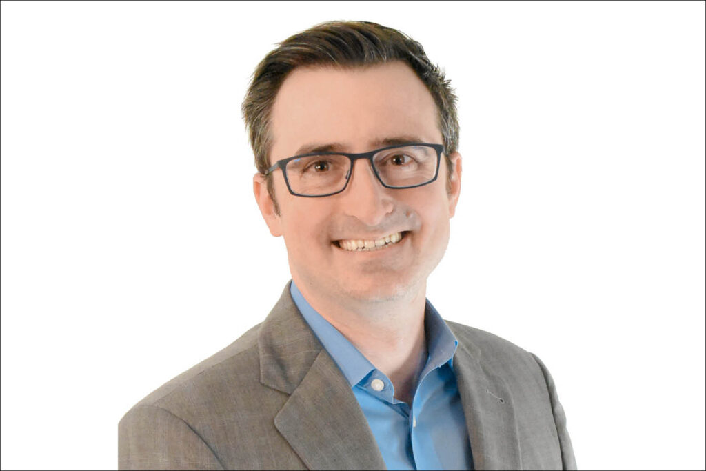 Headshot portrait of a man with glasses smiling in front of a white background