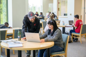 Students collaborating and working around a laptop at an indoor library table