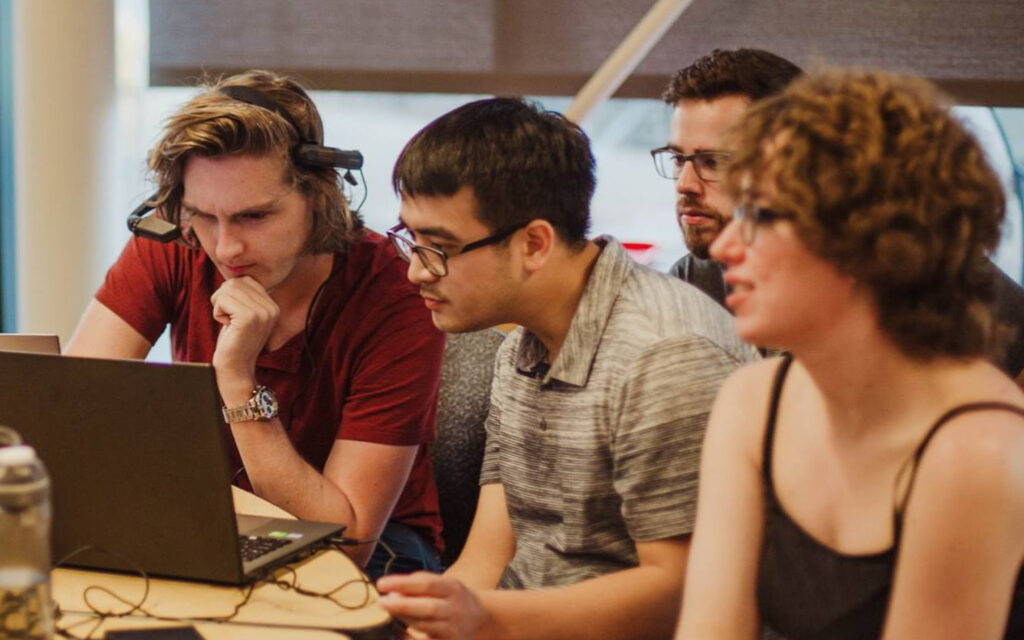 Students gathering closely around computer monitors inside a WSU Vancouver technical lab
