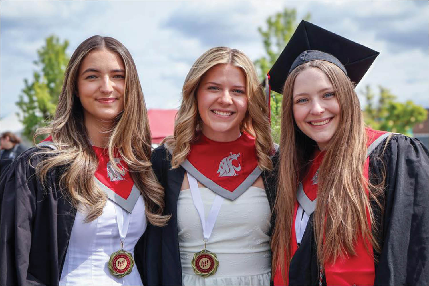 Two female graduates in cap and gown posing together happily